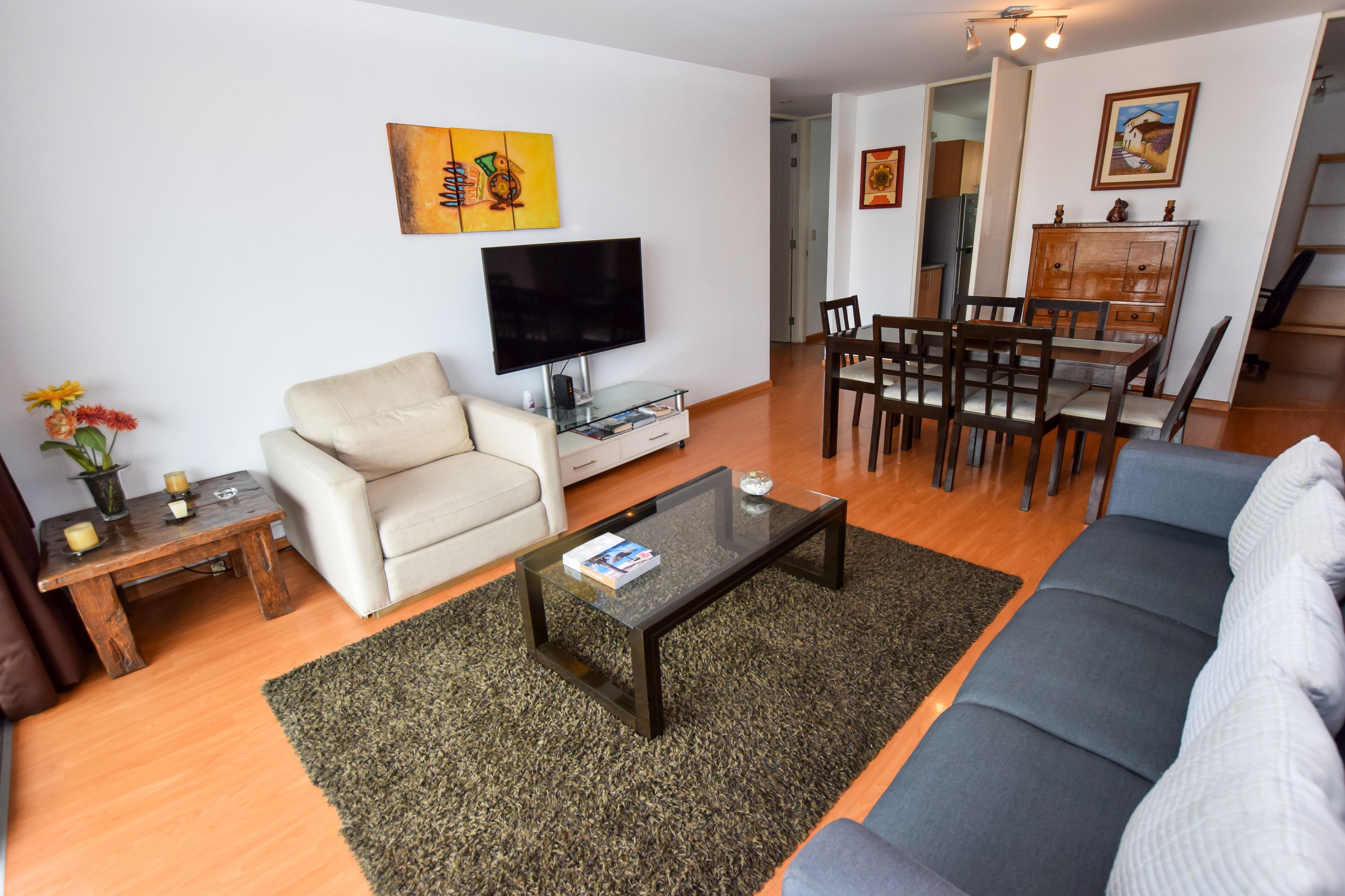 Una sala de estar moderna con un sofá, una mesa de centro, un televisor y un comedor con sillas y una mesa.