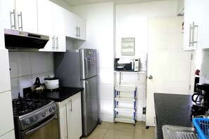 A compact kitchen with white cabinets, a stainless steel stove, a refrigerator, and a microwave. - Miraflores NEST Alcanfores, Near Kennedy Park, 2BR, AC, 1000 Mbps WiFi (Lima)