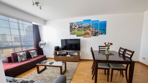 En moderne stue med sofa, sofabord, fjernsyn og et spiseområde med stole og bord.