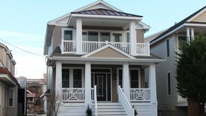 A two-story house with a front porch, a staircase leading to the entrance, and a small front yard. - Upscale New 3BR 2nd Floor Condo • 2 Blocks to Beach • Walk to Boardwalk & Town (Ocean City)