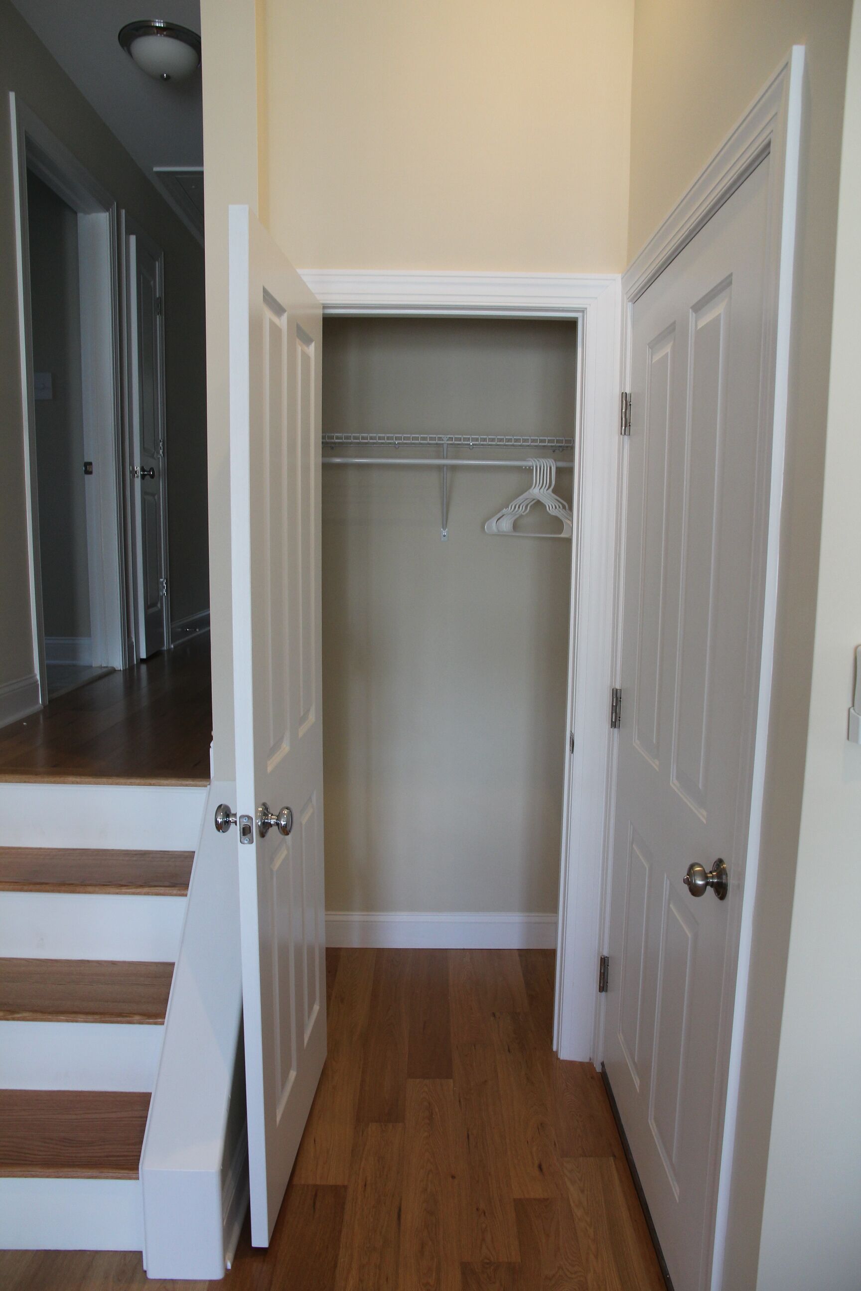 A hallway with a wooden floor, white doors, and a closet with hanging clothes.