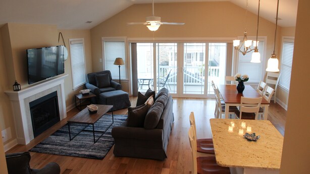 A spacious living room with a fireplace, a large sofa, a dining table with chairs, and a television mounted above the fireplace. - Upscale New 3BR 2nd Floor Condo • 2 Blocks to Beach • Walk to Boardwalk & Town (Ocean City)