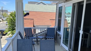 A glass-enclosed balcony with a table and chairs, overlooking a street and neighboring houses. - Upscale New 3BR 2nd Floor Condo • 2 Blocks to Beach • Walk to Boardwalk & Town (Ocean City)