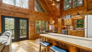 Une cabane en bois avec une grande table à manger, des tabourets de bar et un coin cuisine.