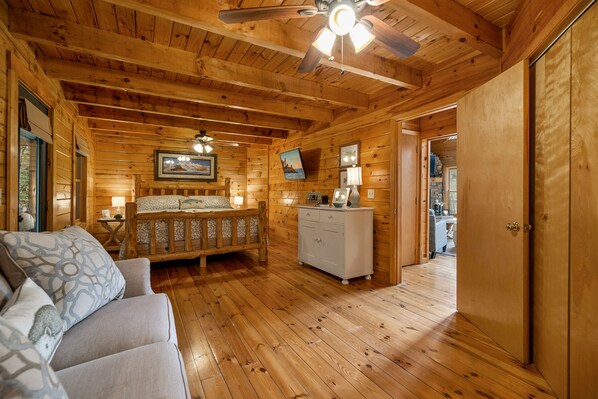 A log cabin bedroom with a wooden ceiling, a bed, a dresser, and a ceiling fan.