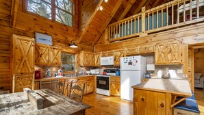 Une cuisine rustique aménagée dans une cabane en bois, avec une table à manger, des placards en bois, un four à micro-ondes, une cuisinière et un réfrigérateur.