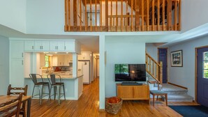 A spacious living area with a kitchen, dining table, and a TV. - Garden Cottage 2.5 Miles to Downtown With Private, Wooded Surroundings (Asheville)