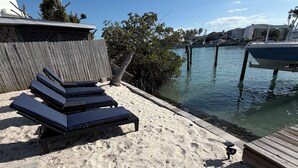 Een zandstrand met ligbedden en een houten terras aan het water.