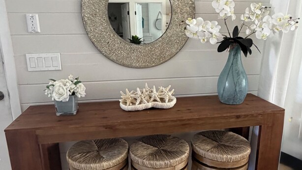 Een houten bar met drie krukken, een ronde spiegel, een vaas met witte bloemen en een decoratieve zeester op het aanrecht.