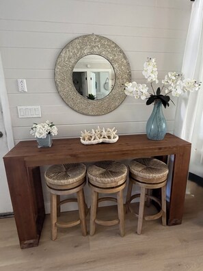 Een houten bar met drie krukken, een ronde spiegel, een vaas met witte bloemen en een decoratieve zeester op het aanrecht.