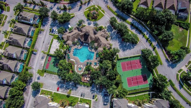 Vista aérea de una zona residencial con piscina central, canchas de tenis y un parque ajardinado.