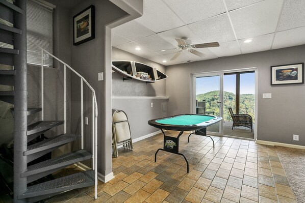 A pool table in a room with a view, a ceiling fan, and a staircase.