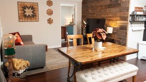 Een gezellige woonkamer met een houten eettafel, een grijze bank en een witte bench.