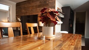 Een houten eettafel met een witte vaas vol rode en gele bloemen, zout- en pepervaatjes en een kaars.