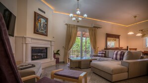 A living room with a fireplace, sofa, and a dining table. - Villa Eleonas (Zakynthos)