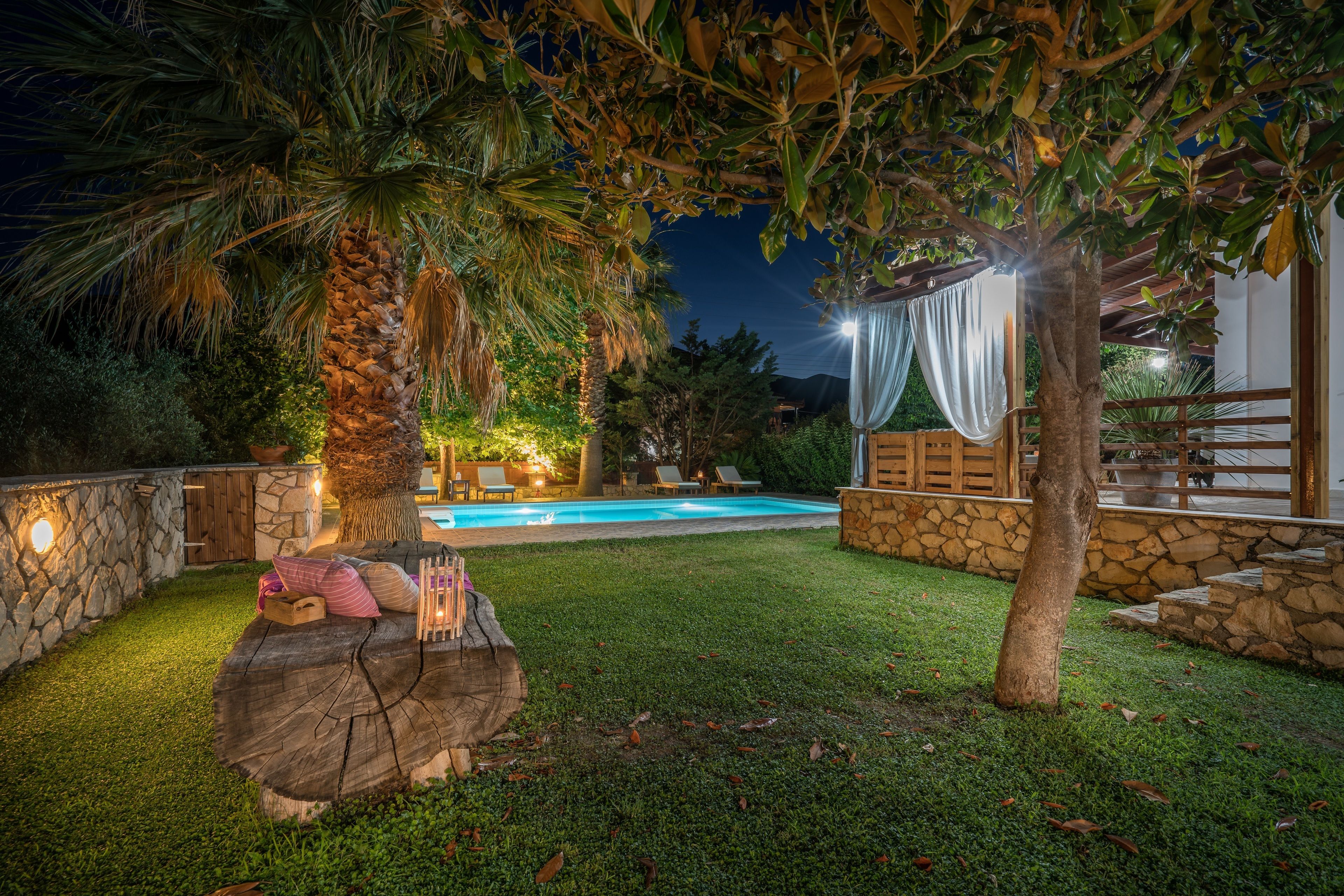 A well-lit outdoor area with a swimming pool, stone walls, and a wooden deck with seating.