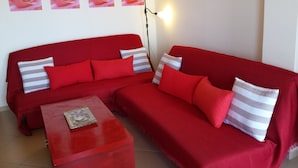 A red sofa with striped pillows, a glass-top coffee table, and a wall with four rose paintings. - Rubini Home III 3 minutes from sea by feet (Chania)