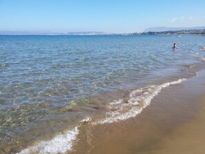 A beach with clear water, a person in the water, and a distant shoreline with buildings. - Rubini Home III 3 minutes from sea by feet (Chania)