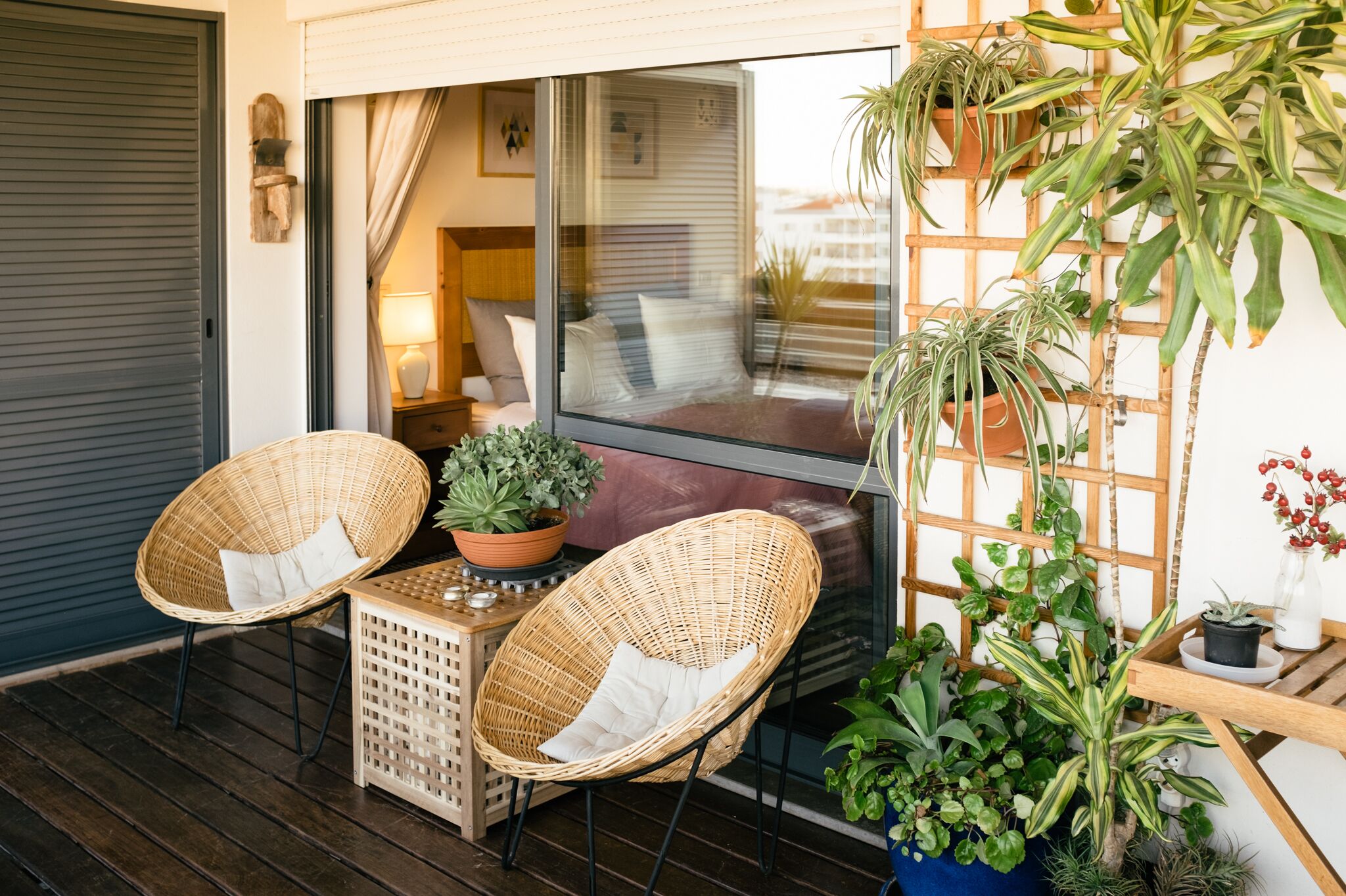 A cozy outdoor seating area with wicker chairs, a small table, and various potted plants.