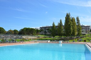 Una piscina con lettini e ombrelloni, circondata da vegetazione e edifici.