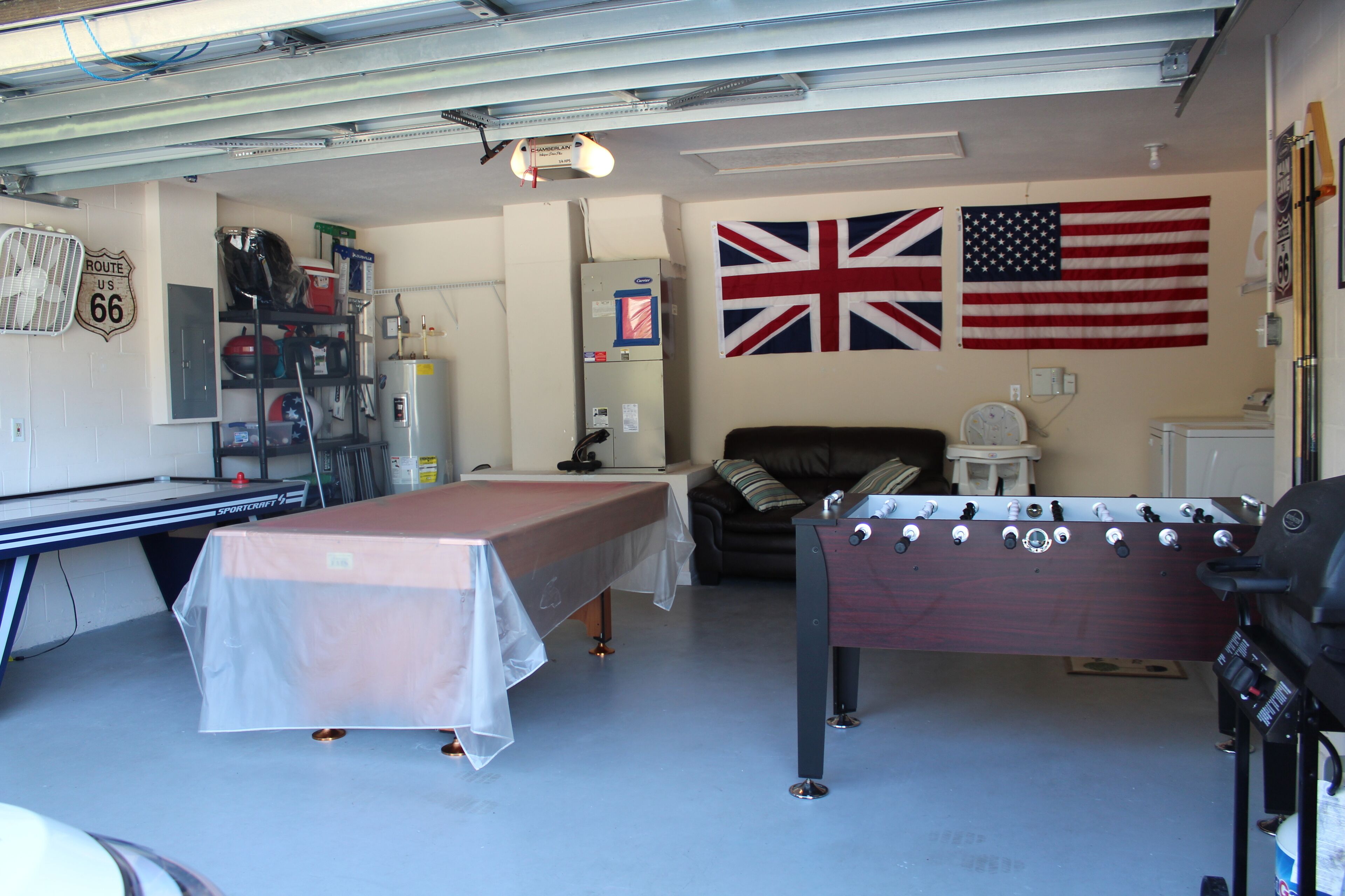A garage with a pool table, foosball table, and a wall with two flags.
