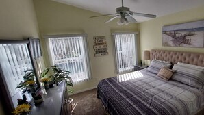 Un dormitorio con una cama, ventilador de techo, un cuadro y una ventana con persianas.