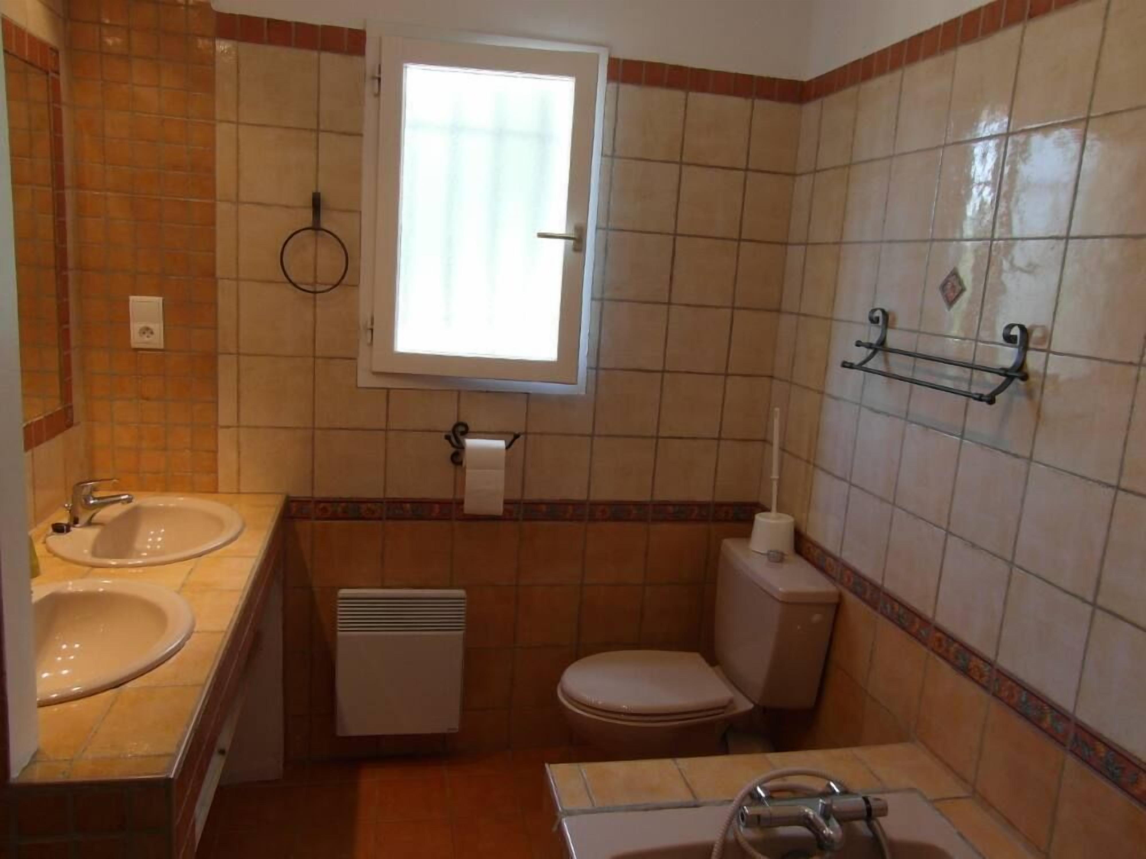 Une petite salle de bain avec un lavabo, des toilettes et une douche. Il y a une fenêtre au-dessus des toilettes et un porte-serviettes au mur.