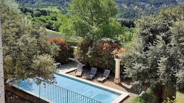 A pool area with lounge chairs and a view of a forested hillside.