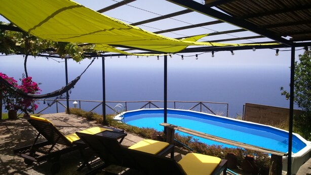 A pool area with a view of the sea, outdoor furniture, and a hammock.