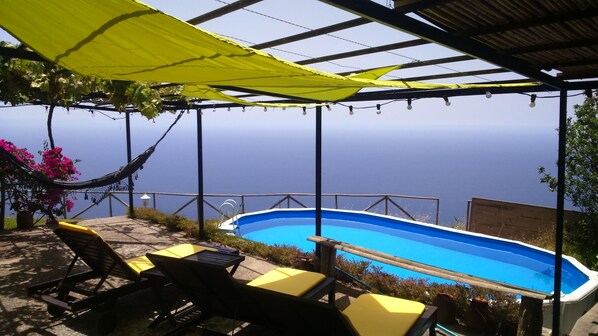 A pool area with a view of the sea, outdoor furniture, and a hammock. - Ocean View Cottage - Stone rocks house with e beautiful ocean view. (Calheta)
