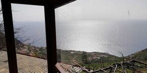 A coastal view from a balcony with a clear view of the sea and a distant village. - Ocean View Cottage - Stone rocks house with e beautiful ocean view. (Calheta)