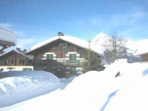 Una cabaña de madera con techo inclinado, rodeada de nieve.