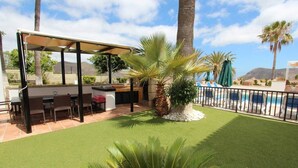 A patio area with a barbecue setup, seating, and a poolside area with lounge chairs. - ViVa Royal (Arona)
