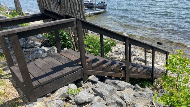 Eine Holztreppe führt zu einem Steg an einem See, umgeben von Felsen und Bäumen.