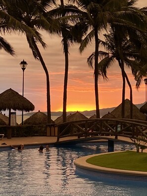Un espace piscine agrémenté de palmiers, avec un coucher de soleil en arrière-plan.
