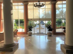A spacious lobby with large windows, columns, and potted plants.