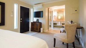 A hotel room with a bed, a desk, a chair, a television, and a bathroom visible through an open door.