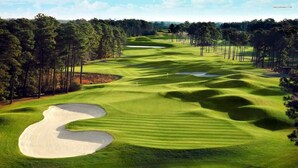 A golf course with sand bunkers, trees, and a clear sky.
