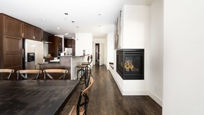 Une cuisine moderne avec des meubles en bois foncé, un réfrigérateur en acier inoxydable, un îlot central doté de tabourets de bar et une cheminée noire.