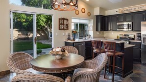 A modern kitchen with dark cabinetry, stainless steel appliances, and a dining area with wicker chairs and a round table.