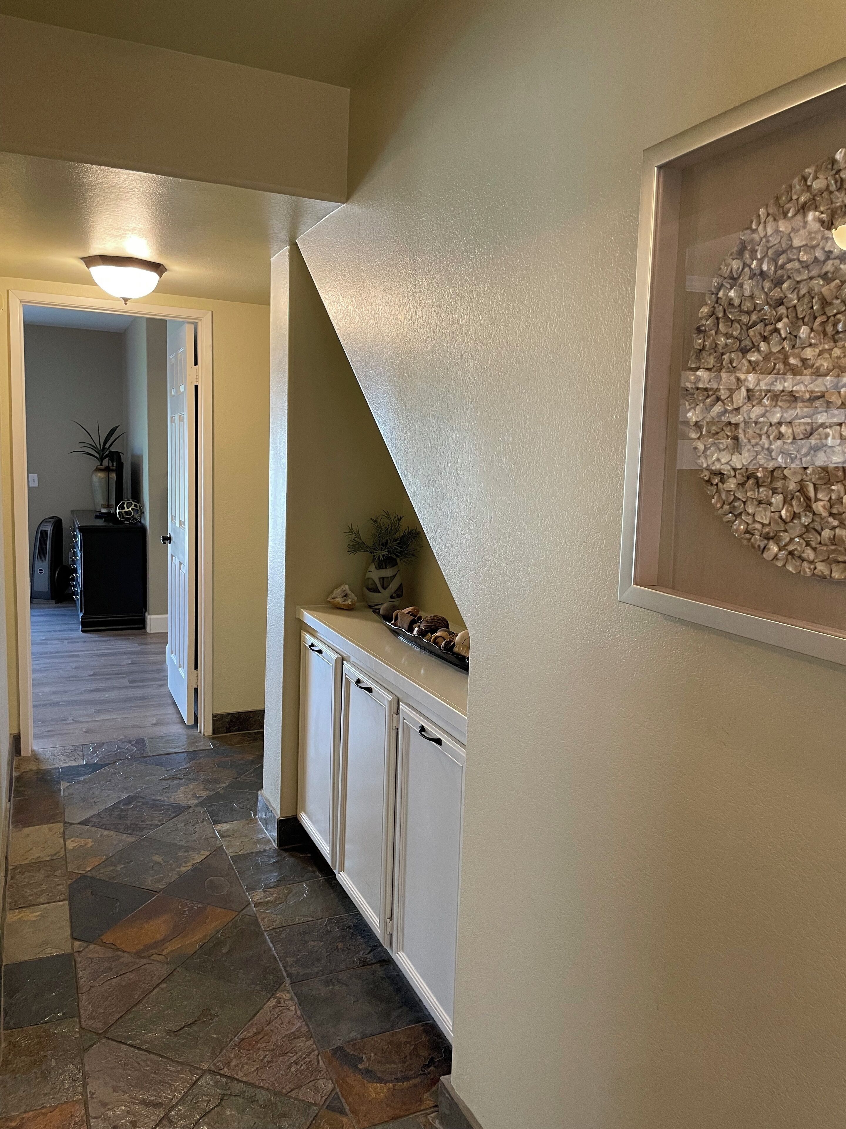 A hallway with a stone tile floor, a white door, and a wall-mounted light fixture.