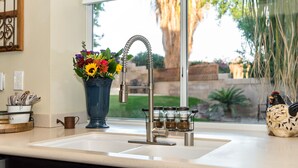 A kitchen with a double sink, a vase with flowers, and a window with a view of a garden.