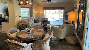 A spacious living area with a round table, wicker chairs, a sofa, and a ceiling fan.