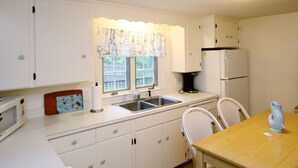 A small kitchen with white cabinets, a sink, a microwave, a refrigerator, and a dining table with two chairs. - 4 Bedrooms, 2 Baths, Sleeps 8-10 (Chatham)