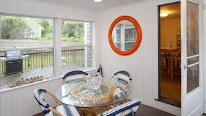 A sunlit room with a glass table surrounded by wicker chairs, a wooden deck visible through a window, and a door leading to another room. - 4 Bedrooms, 2 Baths, Sleeps 8-10 (Chatham)