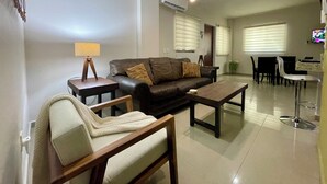 Ein modernes Wohnzimmer mit einer Ledersofa, einem Holztisch, einem beige Armlehnstuhl und einem Essbereich mit Tisch und Stühlen.