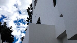Ein modernes Gebäude mit weißer Fassade, zahlreichen Fenstern und blauem Himmel mit Wolken.