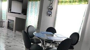 Ruokailutilassa on pyöreä pöytä ja kuusi mustaa tuolia, takka sekä seinälle asennettu televisio.