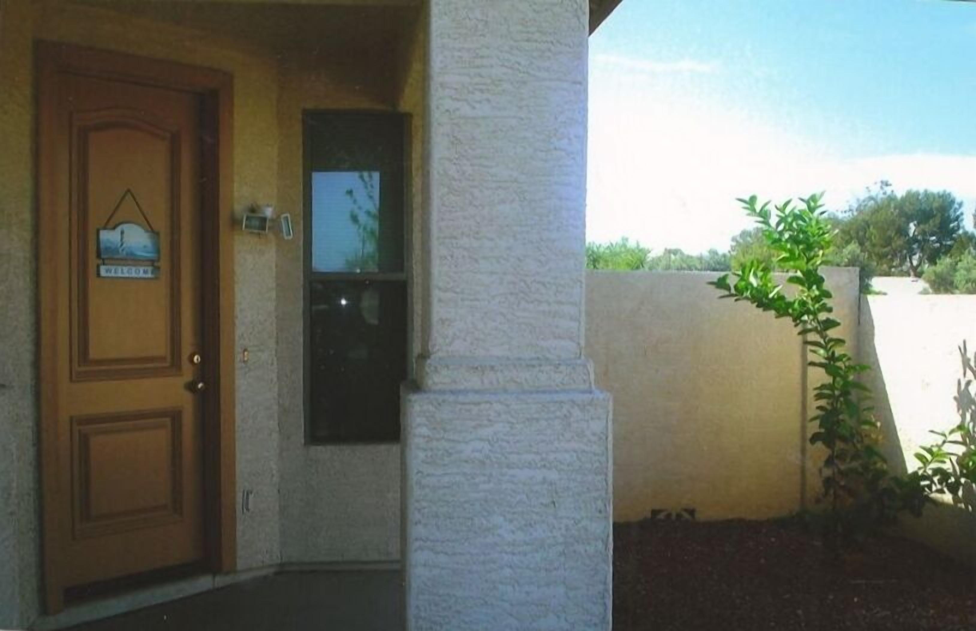 A wooden door with a welcome sign, a small window, and a white pillar.