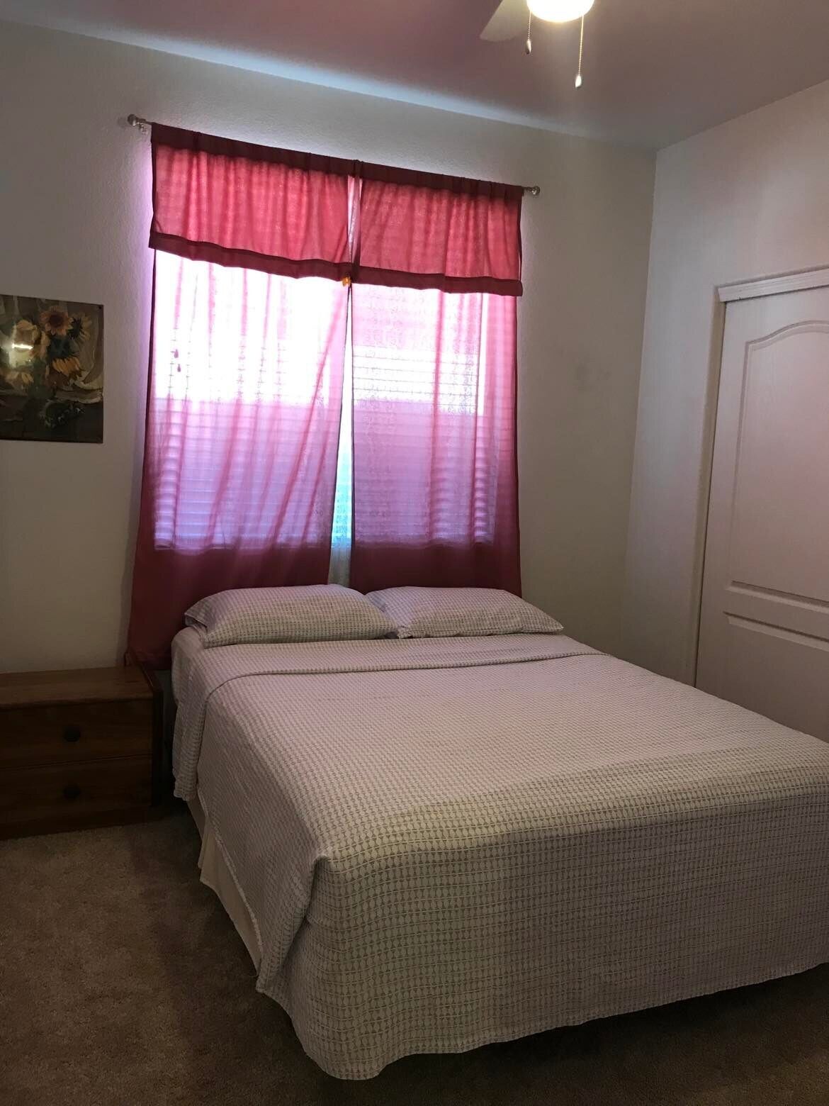 A bedroom with a bed, a nightstand, a door, and a window with curtains.